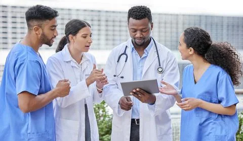 Solving problems as a team. a group of doctors using a digital tablet against a Stock Photos