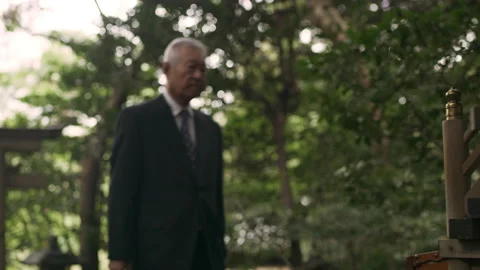 Somber elderly Asian man clapping and bowing in front of a shrine in a beautiful Stock Footage 199459457