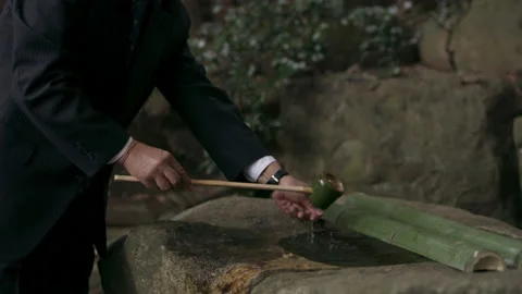 Somber elderly Japanese man taking water from a stone water basin and pouring it Stock Footage 199456152