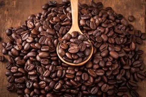 Some coffee bean in spoon of coffee bean heap on the wood table Stock Photos