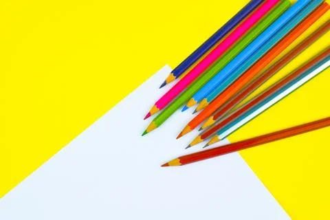 Some different colored pencil crayon scattered across a bright yellow and whi Stock Photos