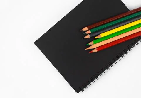 Some different colored pencil crayons scattered on top of a black paper diary Stock Photos