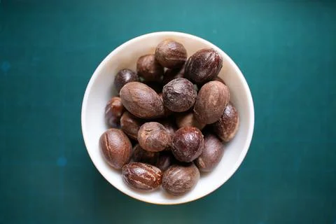 Some dried roasted nutmeg on a ceramic bowl on top of blue background Stock Photos