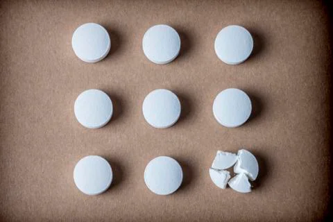 Some isolated white capsules aligned on brown background, conceptual image Stock Photos