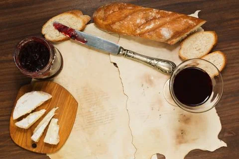 Some meal with red wine, bread, jam and cheese on oldened paper sheets Foto stock