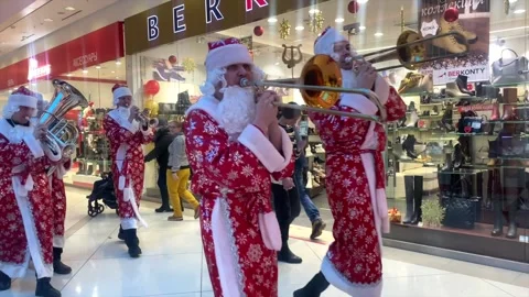 Some Santa Clauses are walking through the mall and playing musical instruments. Stock Footage 170016073