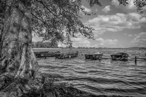 Some several small rowing boats are moored side by side at the edge of a lake Stock Photos