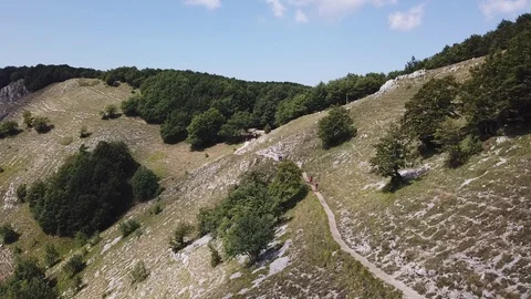 Some trekkers walk on a path in an open mountain valley, aerial view Stock Footage 112993670