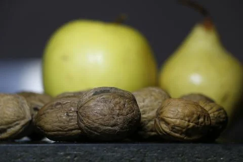 Some walnuts in the foreground an apple and a pear in the background Stock Photos