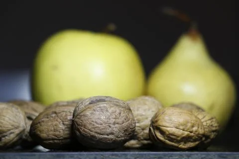 Some walnuts in the foreground an apple and a pear in the background Stock Photos