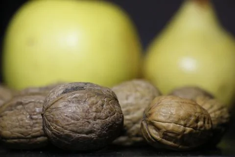 Some walnuts with shell and an apple and a pear in the background Stock Photos