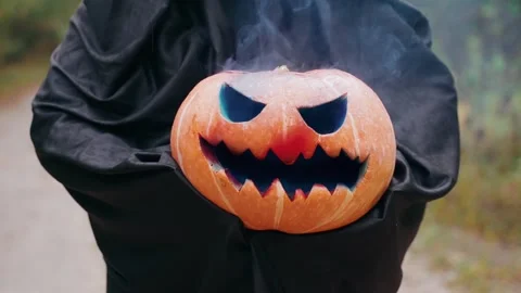 Someone in black holding a Jack O'lantern in the forest blowing blue smoke Stock Footage 253437811