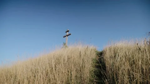 Someone with a camera climbs a hill on which rises a wooden cross Stock Footage 163033218