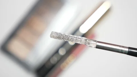 Someone is holding a comb for the eyebrows and a background of a blurry set of Video stock 90490961