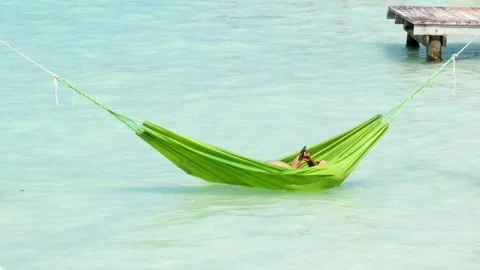 Someone is lying in a green hammock over the sea and using a mobile phone Stock Footage 240021654