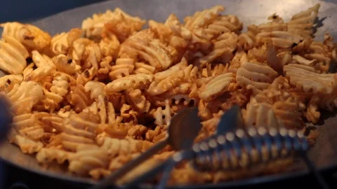 Someone serving themself waffle fries from a serving bowl closeup Stock Footage