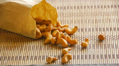 Someone throws a paper bag of cashew nuts on a bamboo napkin on the table Video stock 67639396