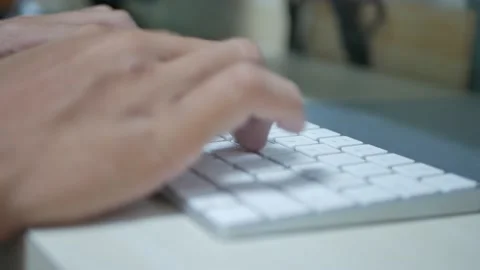Someone's hand is fast touch typing on white flat keyboard on a wooden table Stock Footage 211591936