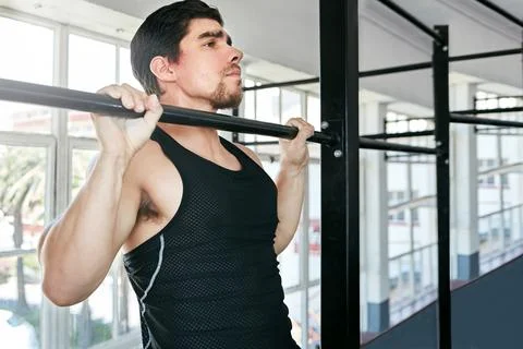 Sometimes the basic exercises are best. a young man doing pull ups in a gym. Stock Photos