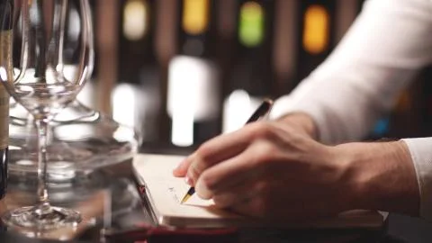 Sommelier keeps notes in a notebook against the background of shelves with wine Stock Photos