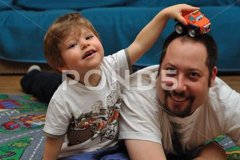 Son and father playing with cars on carpet at home Stock Photos