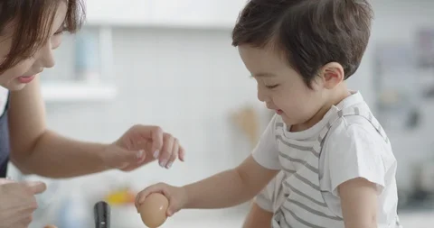 Son and mother breaking eggs to cook Stock Footage 100943561