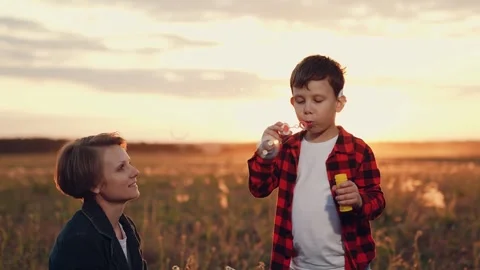 Son blows soap bubbles standing in field with growing plants near mother Stock Footage 257179558