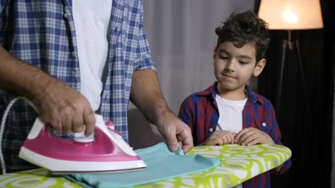 Son helping dad to fold ironed clothes at home Stock Footage 100727595