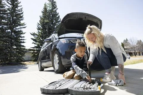 Son helping mother select tool from toolbox in driveway Photos