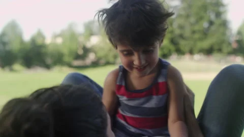 A son laughs and smiles while playing with his mother on a sunny day at the park 스톡 동영상 143628322