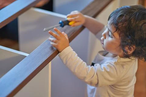 Son plays with screwdriver while his father assembles wooden furniture at hom Stock Photos