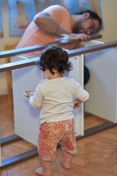 Son plays while his father assembles wooden furniture at home. Carpentry and  Stock Photos
