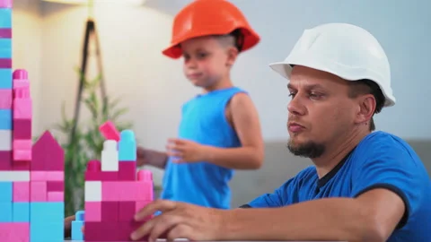 Son runs to a father playing bricks construction game on table with his son in Stock Footage 132522212