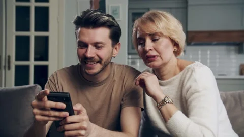 Son showing his elderly mum how to upload new photo using smartphone. A young Stock Footage 265667757