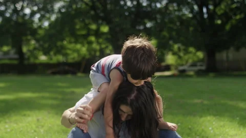Son sitting on the shoulders of his young mom while sitting on the grass Stock Footage 143620106