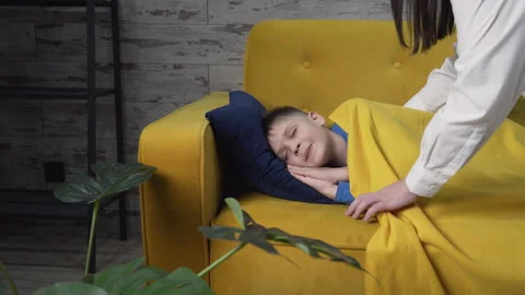 Son is sleeping on the sofa mom comes up to him and covers him with a blanket Stock Footage 261060921