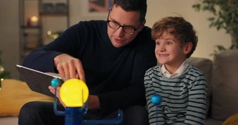 Son is spending time with dad men are sitting on couch playing with a model of Stockbeeldmateriaal 210469572