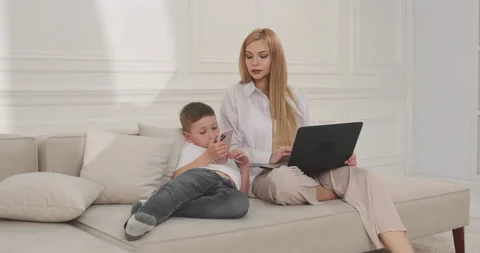 The son studies online using the phone and the mother works on a laptop. Video stock 203794239