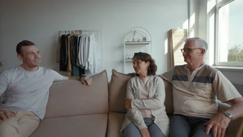 Son talks to elderly parents sitting on sofa in living room Stock Footage 201352576