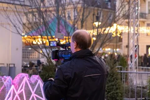 Sony camera operator filming at a festive winter market with twinkling street Stock Photos