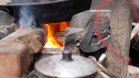A soot covered cooking pot stands above an open fire inside a clay stove with wa 스톡 동영상 341408449