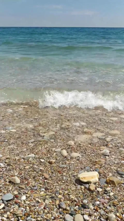 Soothing vertical view of small waves rolling onto a pebble shore Stock Footage 312778911