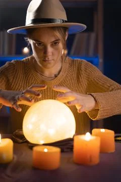 Soothsayer using crystal ball to predict future at table in darkness with can Stock Photos