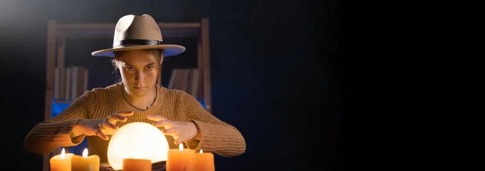 Soothsayer using crystal ball to predict future at table in darkness with can Stock Photos