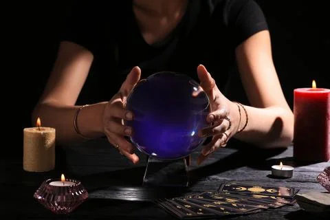 Soothsayer using crystal ball to predict future at table in darkness, closeup Foto stock