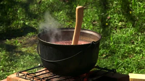 Soup is boiling in a Black Cauldron on the Fire. Ax Instead of a Cup Stock Footage 257973502