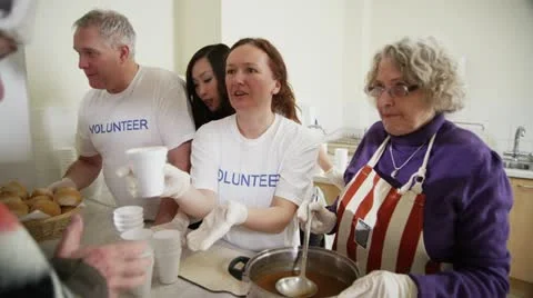 Soup kitchen volunteers help to feed the homeless Stock Footage