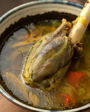 Soup with meat on bone. Close up. Serving of rich broth with boiled meat and Stock Photos