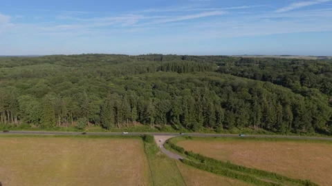 South of England,flight over green fields towards forest edge road in the Stock Footage 345226402