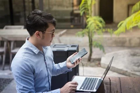 Southeast asian young man using his smartphone and laptop computer in a cafe Stock Photos
